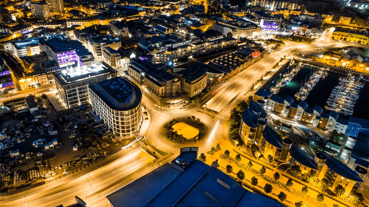 Aerial view at night of a town's lit streets, a roundabout and a marina full of boats
